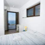 Camera da letto con letto matrimoniale e vista mare, arredi minimal e luce naturale – Villa Giardino degli Ulivi, Sicilia