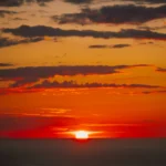 Sole che tramonta sull’orizzonte marino, con il cielo tinto di rosso, arancio e oro sopra il Mar Tirreno.