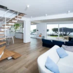 Salotto open space con divani, scala in legno e vista su uliveto e mare – Villa Giardino degli Ulivi, Sicilia