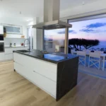 Cucina moderna con isola centrale e ampia vetrata sul tramonto e vista mare – Villa Giardino degli Ulivi, Sicilia