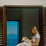 Donna che legge un libro seduta sulla finestra di Villa Giardino degli Ulivi, con vista sull’isola di Alicudi.