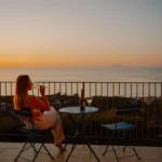 Donna che sorseggia un bicchiere di vino bianco al tramonto sulla terrazza di Villa Giardino degli Ulivi, con vista su Alicudi.