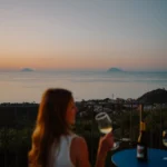 Donna con bicchiere di vino bianco al tramonto sulla terrazza di Villa Giardino degli Ulivi a Capo d’Orlando, con vista sulle isole di Alicudi e Filicudi.